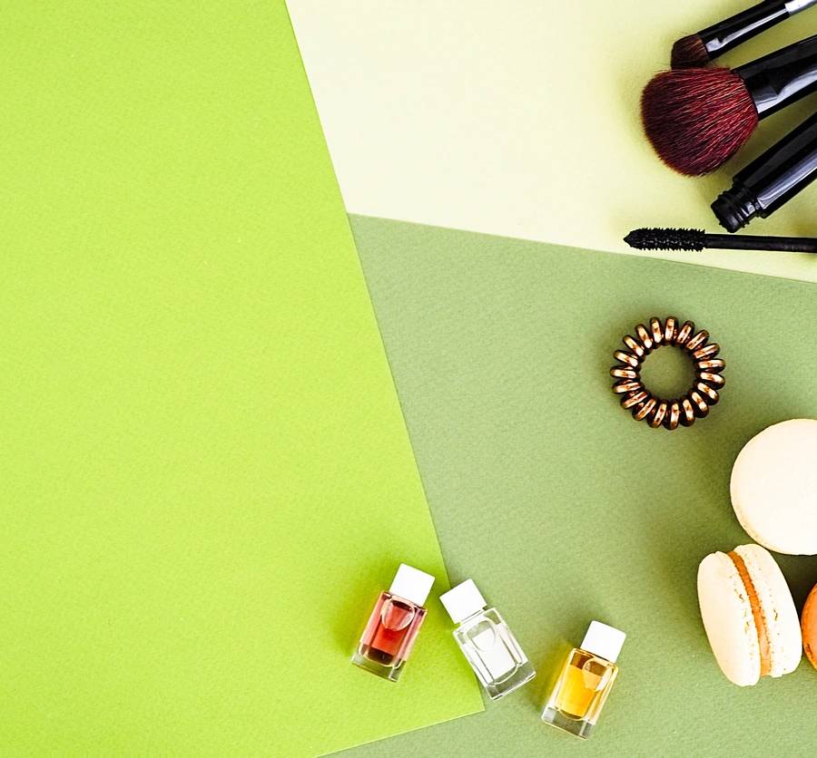 Flat lay for fashion blog and social media. Woman's glamour beauty accessories and tools on a colorful greenery background. Perfumes, brushes, mascara, blushes, spiral hair tie, macaroons. Copy space for text. Horizontal (Flat lay for fashion blog an